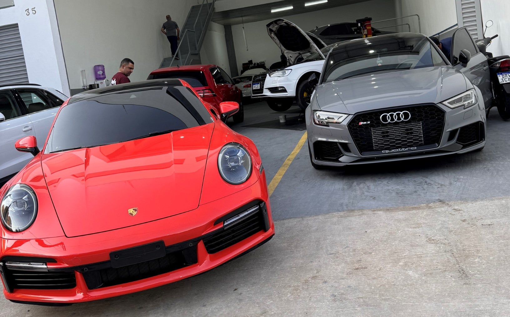 A BMW Sedan with a roof rack is parked in a field with a young woman admiring it over her shoulder in the foreground.
